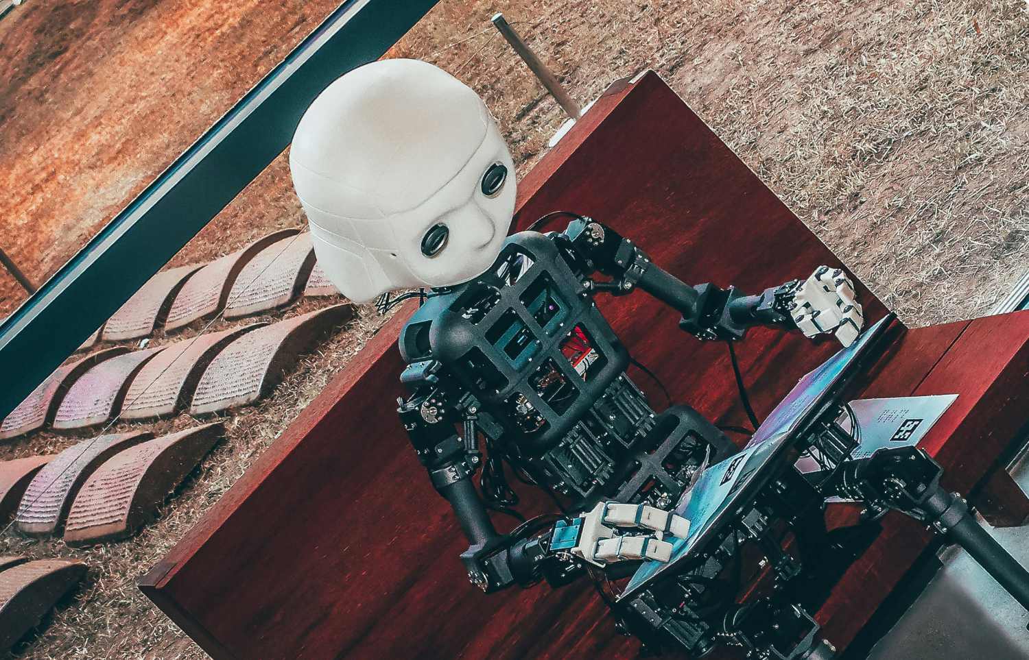 A robot sitting on a bench with his head down, looking at a book, trying to decipher the words