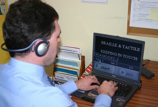 Man wearing headset typing on laptop running JAWS screen reader.