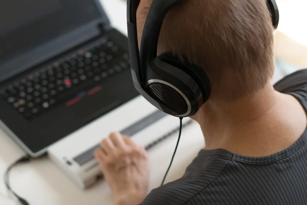 Person wearing headphones using laptop with refreshable Braille display.