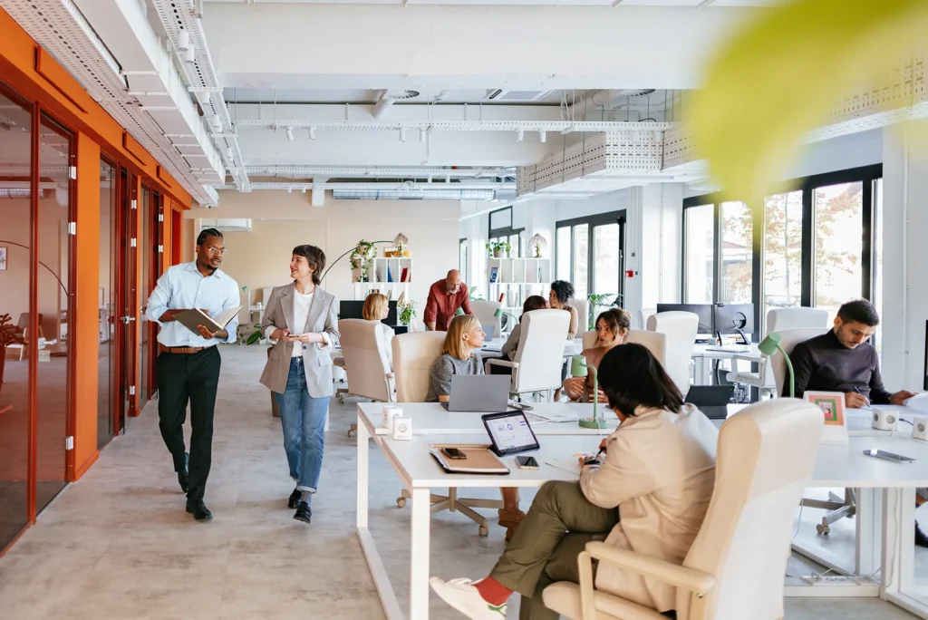 Modern collaborative office space with with diverse professionals seated at desks and walking and talking.