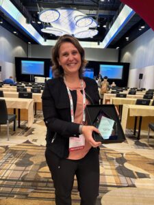 Carolina smiling and holding the glass Spirit of Accessibility Award trophy.